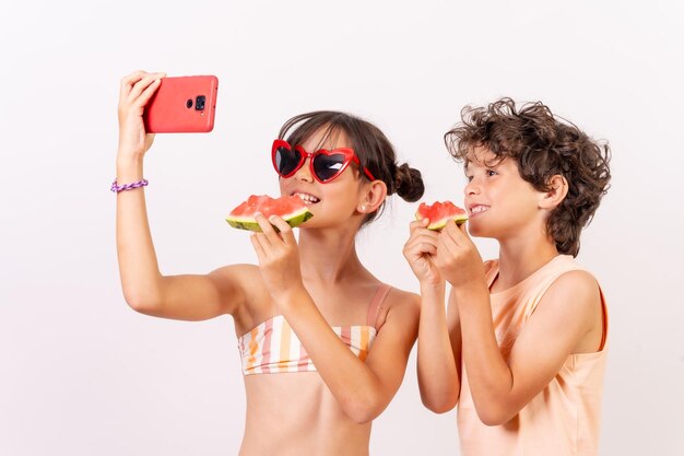 Children enjoying the summer eating a watermelon taking a selfie with the phone White background