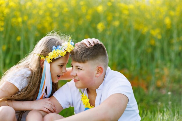 天気の兄と妹を楽しんでいる子供たちはスクワットに座って、空の下で花や草とフィールドで話します