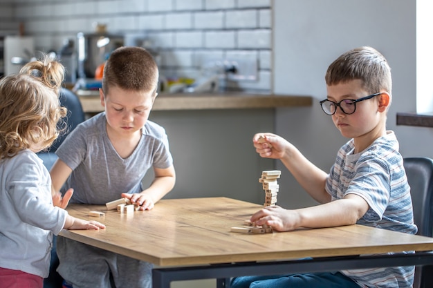 Children enthusiastically play a board game with wooden cubes on the table.