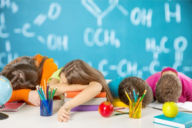 Children fall asleep on table while doing homework on classroom background