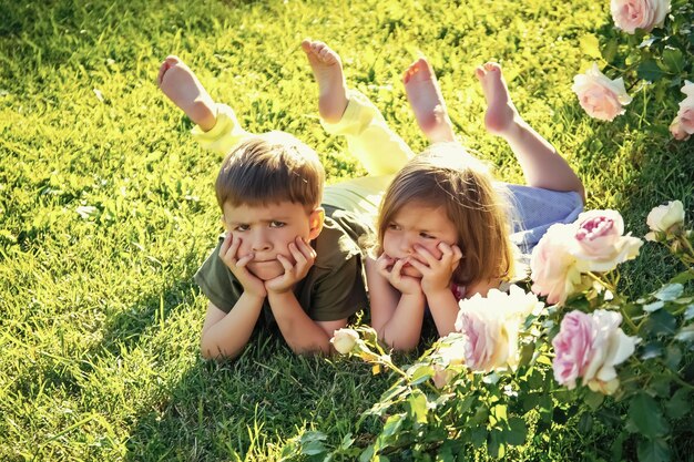 Children Friends and friendship concept Kids lying on green grass in summer garden Childhood leisure and fun Boy and girl at blossoming rose flowers on lawn Growth and flourishing