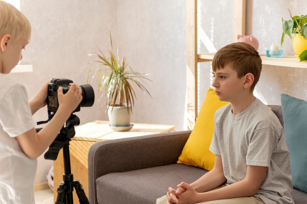 Children friends record videos on camera in the Livingroom. Teenage boy takes vlog. Child blogger.