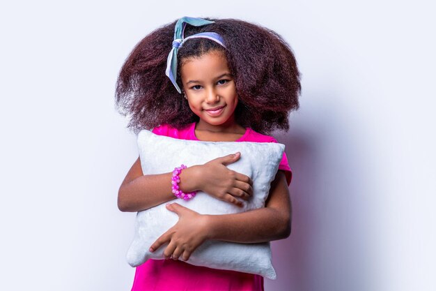 Children girl holding a pillow on a white background Smiling multiracial kid girl holding cushion Smile little african american girl hold kissen Morning little girl pillow cushion kissen