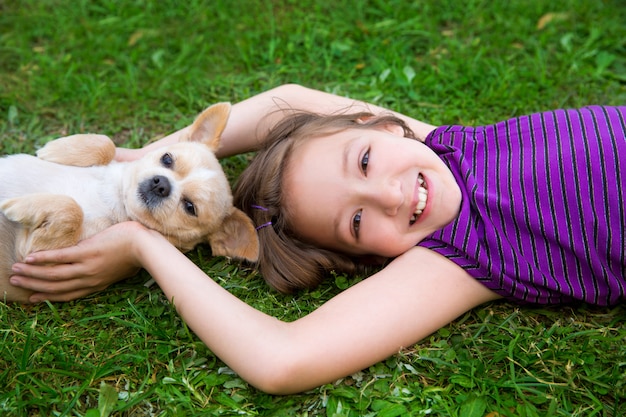 Ragazza dei bambini che gioca con il cane della chihuahua che si trova sul prato inglese