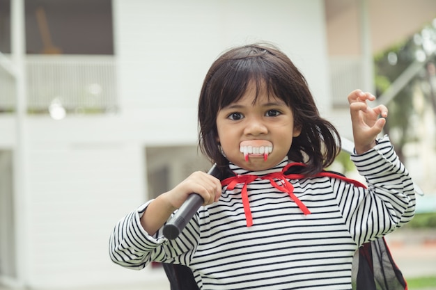 Children girl wearing mysterious Halloween dress holding a sickle on white background