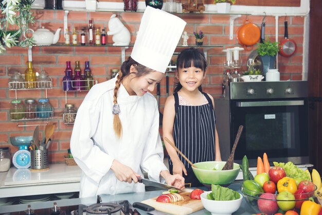 Children girl and woman chef smiling in kitchan room