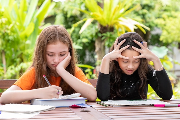 Ragazze dei bambini che fanno i compiti e si riuniscono in giardino a casa pensando seriamente alla soluzione