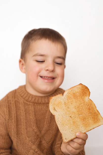 子供とグルテン。トーストしたパンを持つ就学前の男の子。子供によるグルテン不耐性。テキストまたは記号用のパンのスペースをコピーします。