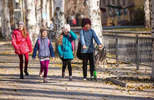 Дети ходят в школу на тротуаре с веселой компанией.