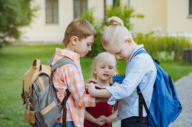 晴れた日にバックパックを持って学校に行く子供たち。学年の始まり。男の子と女の子、学校の玄関先でホームフークをチェック