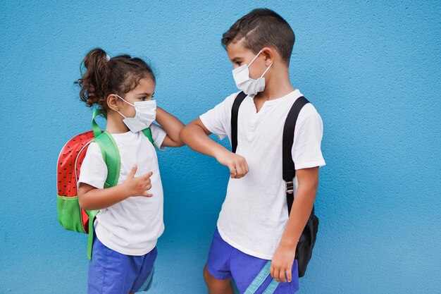 Дети приветствуют друг друга ударом локтя и надевают защитную маску, возвращаясь в школу.