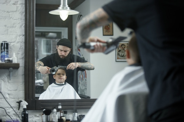 Children hairdresser cutting little boy against a dark background. Contented cute preschooler boy getting the haircut.