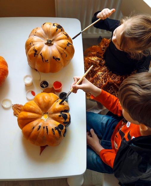 Children in Halloween costumes paint pumpkins Boy and little girl decorate the house for holiday