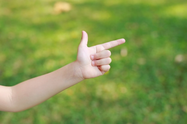 Children hand pointing with index finger or making gun gesture on blur green garden. Kid hand show up forefinger correct or point.