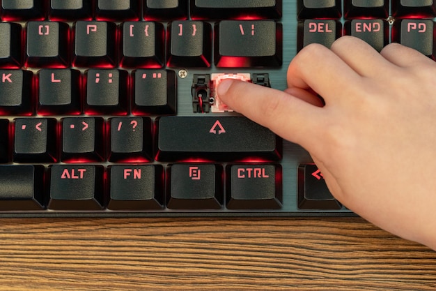 Children hand presses a broken enter button on a black keyboard\
with red backlight