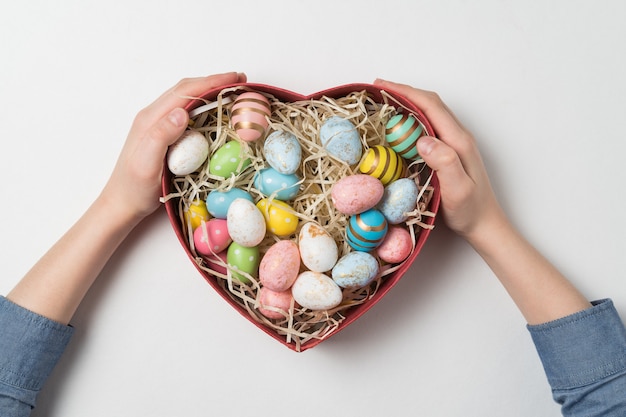 Children hands holding heart shaped box with Easter eggs.