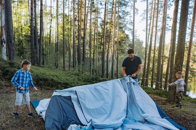 Дети помогают отцу поставить палатку Концепция семейного кемпинга