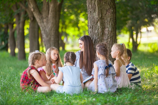 Children hold a lesson with the teacher in the park on a green lawn.