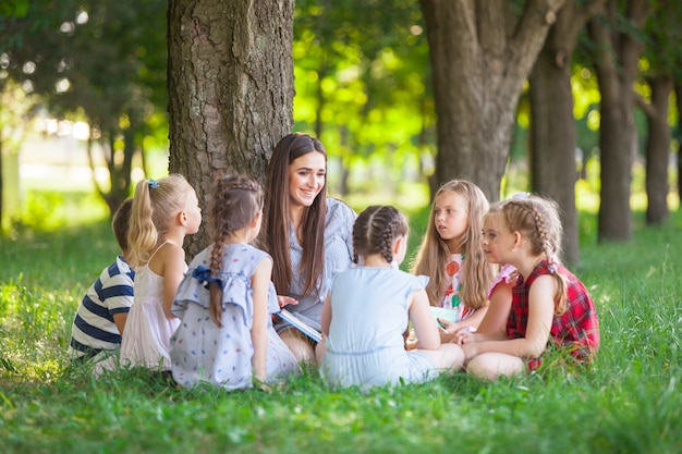 Children hold a lesson with the teacher in the park on a green lawn.