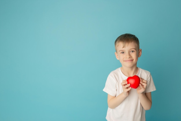 Bambini che tengono il cuore rosso su sfondo blu concetto di amore cura fede speranza purezza luogo per il testo mosca piatta