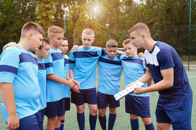 Children hugs and listening to explain of coach with clipboard in hands