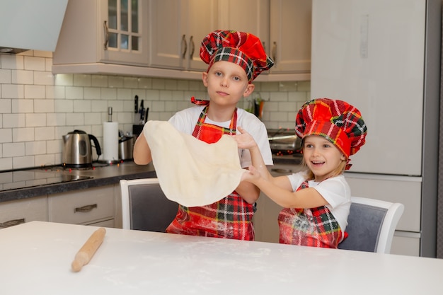 요리사 의상을 입은 아이들이 크리스마스 쿠키를 만들기 위해 롤링 핀으로 반죽을 펼치고 있습니다.