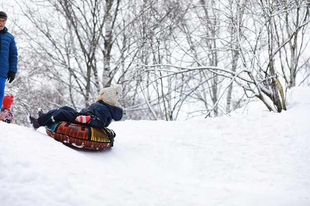 写真 冬の公園の子供たち 遊び場で雪遊びをする子供たち 雪だるまを作って丘を滑り降りる