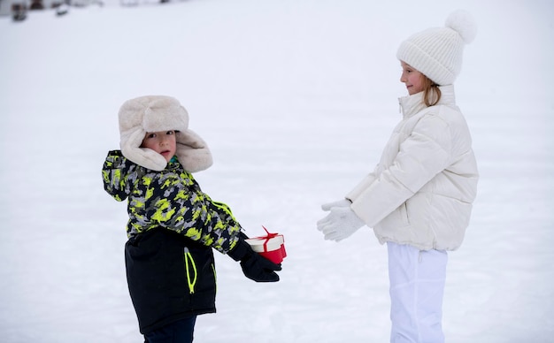 写真 雪の中の子供たち 冬服を着た小さな男の子が小さな女の子にハートの形で贈り物をする