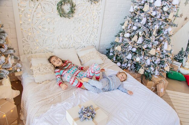 Children jump on the bed near the christmas tree selective\
focus