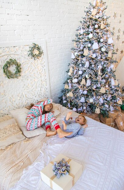 Children jump on the bed near the christmas tree selective\
focus