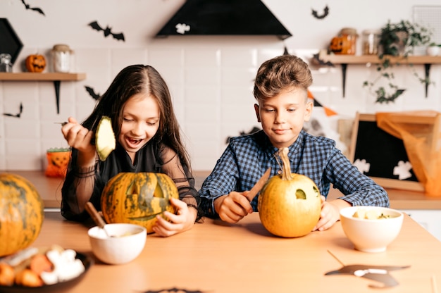 Children in the kitchen are carving a pumpkin for Halloween Halloween holiday and family lifestyle