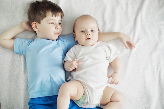 Children lie on the bed next to the newborn baby, little sister. Children's emotions.