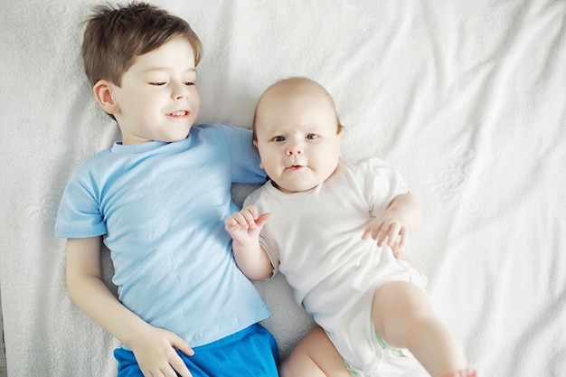 Children lie on the bed next to the newborn baby little sister