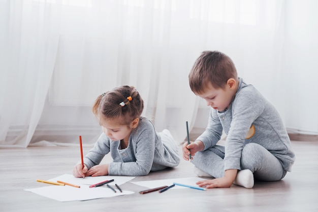 Children lie on the floor in pajamas and draw with pencils. Cute child painting by pencils