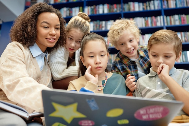 Children looking at laptop screen with smiling teacher