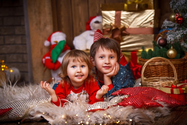 children lying on the skin in a Santa hat next to the Christmas tree