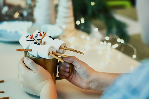 Children make snowmen from marshmallows and salted straws drink cocoa in the home kitchen preparing ...