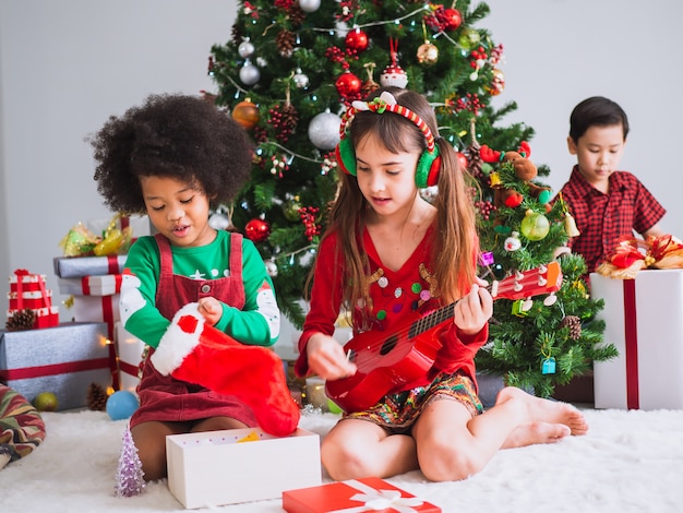 Foto i bambini di molte nazionalità festeggiano il giorno di natale, i bambini sotto l'albero di natale suonano la chitarra