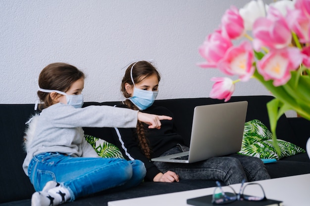 Children in medical masks studying homework during online lesson at home