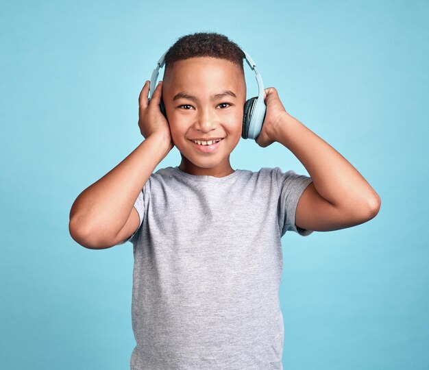 Children music and headphones with a boy listening to the radio or streaming audio in a studio on a blue background Kids online and track with a young male child enjoying a song with technology