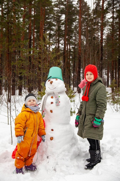 冬の9歳と3歳の子供たちは雪だるまの近くを歩きます