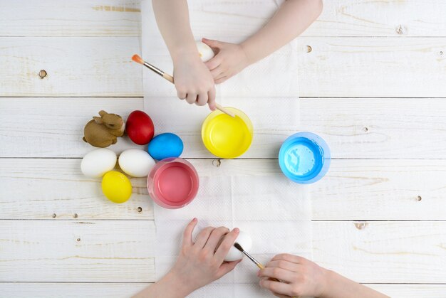 Children paint eggs for Easter on the wooden table