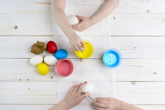 Children paint eggs for Easter on the wooden table
