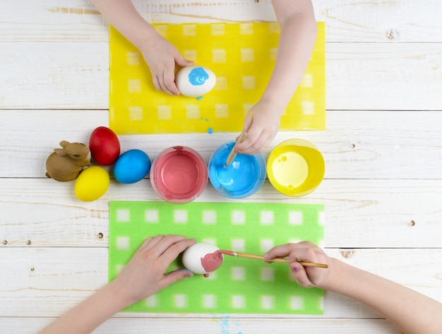 Children paint eggs for Easter on the wooden table