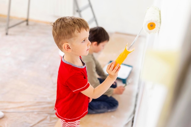 Photo children paint a wall with brush and roller in white color children paint wall