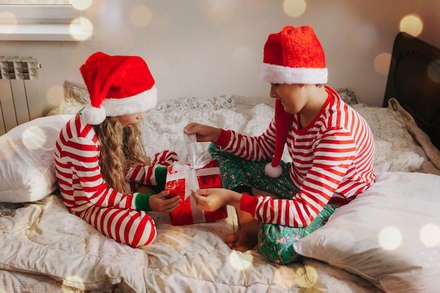 Children in pajamas and christmas hats on the bed with gifts. christmas and new year concept