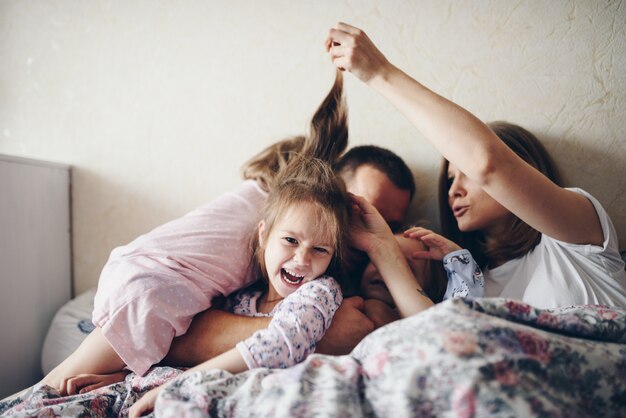 子供と親は朝ベッドで休む。子供たちはふける、抱擁します。双子。 3人の娘。