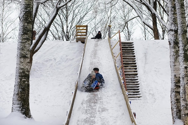 冬の公園の子供たち 遊び場で雪遊びをする子供たち 雪だるまを作って丘を滑り降りる