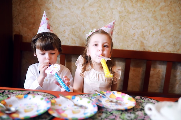 Children party in caps celebrating birthday with cake and balloons at home.