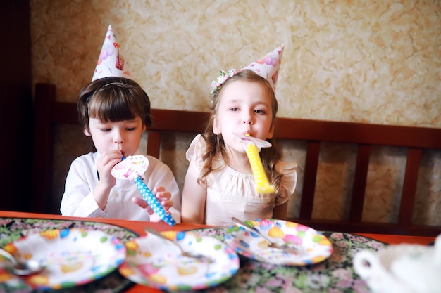 家でケーキと風船で誕生日を祝う帽子をかぶった子供たちのパーティー。